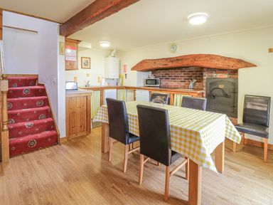 A kitchen dining area with wooden floor a table with checkered tablecloth and black chairs stairs with red carpet at Daffodil Cottage in Caeathro near Caernarfon