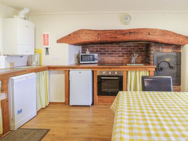 A kitchen with wooden counters a microwave a small refrigerator an oven a dishwasher and a table with a yellow checkered tablecloth at Daffodil Cottage in Caeathro near Caernarfon