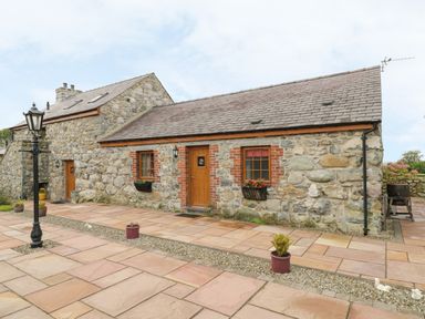 A stone cottage with wooden doors and windows surrounded by a stone patio with potted plants and a lamp post at Daffodil Cottage in Caeathro near Caernarfon