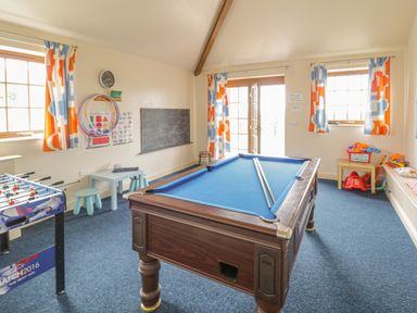 A game room with a pool table foosball table small stools and colorful curtains at Daffodil Cottage in Caeathro near Caernarfon