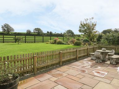 A fenced patio with stone table and chairs next to a garden and green field at Daffodil Cottage in Caeathro near Caernarfon