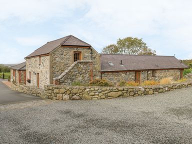 A stone building with a gravel driveway and a stone wall at Daffodil Cottage in Caeathro near Caernarfon