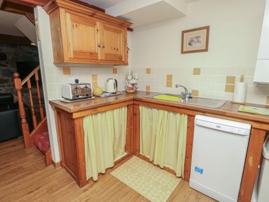 A kitchen with wooden cabinets and appliances at Daffodil Cottage in Caeathro near Caernarfon