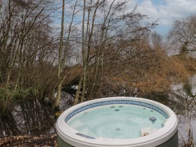 An outdoor hot tub near a body of water surrounded by leafless trees at The Lakeside Yurt in Beckford