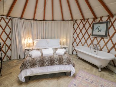 A bedroom with a bed a fur throw white curtains and a bathtub at The Lakeside Yurt in Beckford