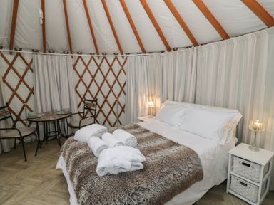 A bedroom inside a yurt with a bed with white linens and fur throw and small dining table with two chairs at The Lakeside Yurt in Beckford