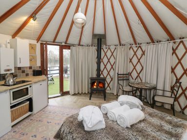 An interior view of a yurt with a bed covered in towels a small kitchen area a wood stove and a dining table with two chairs at The Lakeside Yurt in Beckford