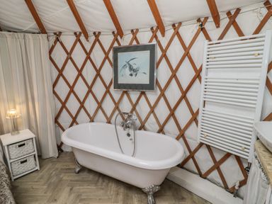 A bathroom with a freestanding bathtub a white radiator a small cabinet with two woven drawers and a framed picture on the wall at The Lakeside Yurt in Beckford