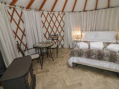 A yurt interior with a double bed with rolled towels a small round table with two chairs and a wood stove at The Lakeside Yurt in Beckford
