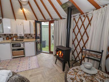 A kitchen and dining area with a stove fire and an open door leading outside at The Lakeside Yurt in Beckford