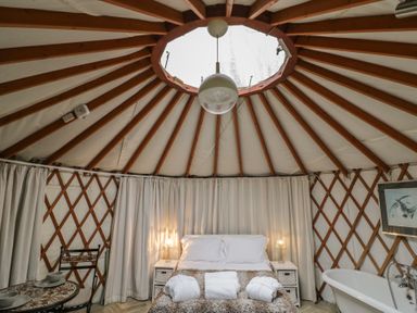 A bedroom inside a yurt with a bed between two bedside tables and a bathtub at The Lakeside Yurt in Beckford