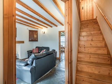 A living room with black leather sofas and wooden ceiling beams next to wooden stairs at Ty Capel Jeriwsalem in Bronaber near Trawsfynydd