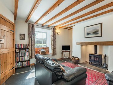 A sitting room with leather sofas a wood stove and a bookshelf at Ty Capel Jeriwsalem in Bronaber near Trawsfynydd