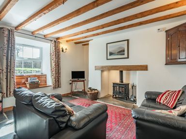 A living room with a wood burning stove black leather sofas and a red rug at Ty Capel Jeriwsalem in Bronaber near Trawsfynydd