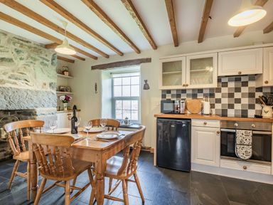 A kitchen with wooden dining table and chairs stone wall and tiled backsplash at Ty Capel Jeriwsalem Bronaber near Trawsfynydd
