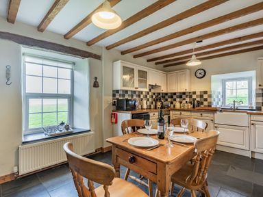 A kitchen with wooden table set for four and white cabinets with checkered backsplash at Ty Capel Jeriwsalem in Bronaber near Trawsfynydd