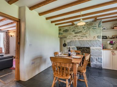 A dining area with a wooden table and chairs set with plates and wine glasses in front of a stone fireplace at Ty Capel Jeriwsalem in Bronaber near Trawsfynydd