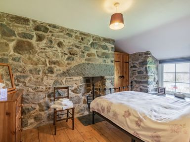 A bedroom with a stone wall a wooden dresser a chair with towels a bed and a window at Ty Capel Jeriwsalem in Bronaber near Trawsfynydd