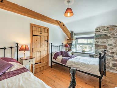 A bedroom with two single beds wooden door bedside tables with lamps and a window at Ty Capel Jeriwsalem in Bronaber near Trawsfynydd
