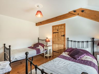 A bedroom with two single iron beds with purple bedding a wooden door and exposed wooden beams at Ty Capel Jeriwsalem Bronaber near Trawsfynydd