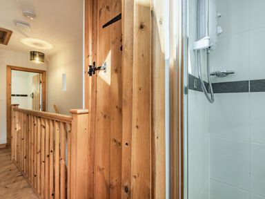 A wooden staircase railing and door near a tiled shower in a hallway at Ty Capel Jeriwsalem in Bronaber near Trawsfynydd