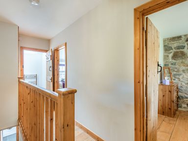 A hallway with wooden railings and doors leading to rooms with wooden furniture and stone wall at Ty Capel Jeriwsalem in Bronaber near Trawsfynydd