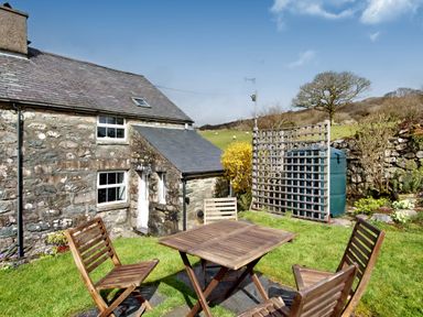 A stone cottage garden with wooden table and four chairs and a water tank at Ty Capel Jeriwsalem Bronaber near Trawsfynydd