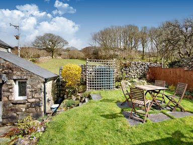 A garden with wooden table and chairs on grass next to stone cottage and stone wall at Ty Capel Jeriwsalem in Bronaber near Trawsfynydd