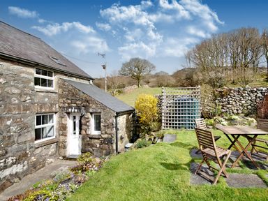A stone house with white doors and windows and a garden with wooden table and chairs at Ty Capel Jeriwsalem in Bronaber near Trawsfynydd