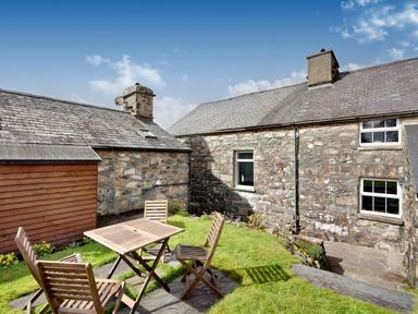 An outdoor patio with a wooden table and four chairs on grass beside stone buildings at Ty Capel Jeriwsalem in Bronaber near Trawsfynydd