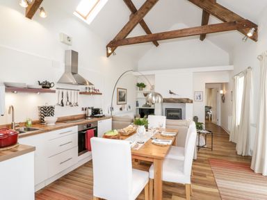 Kitchen and dining area with wooden table white chairs and exposed wooden beams at Beudy Hywel in Llanrug near Llanberis