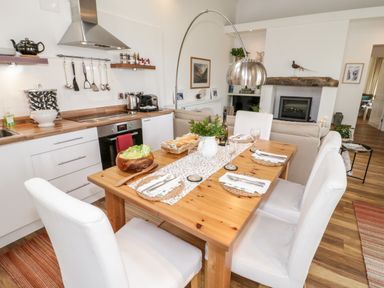 A kitchen and dining area with a wooden table set for four and white chairs at Beudy Hywel in Llanrug near Llanberis