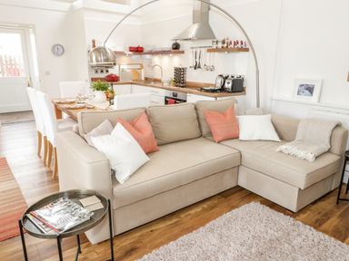 A beige sectional sofa with pillows in an open-plan living room and kitchen at Beudy Hywel in Llanrug near Llanberis