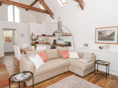 An open plan living room and kitchen with a beige sofa dining table and kitchen appliances at Beudy Hywel in Llanrug near Llanberis