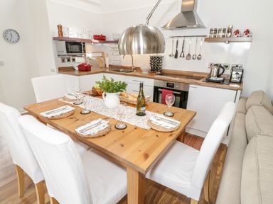 A kitchen and dining area with a wooden table set for four and a sofa at Beudy Hywel in Llanrug near Llanberis
