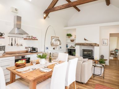 An open plan kitchen and dining area with a wooden table set for four and a living area with a fireplace at Beudy Hywel Llanrug near Llanberis