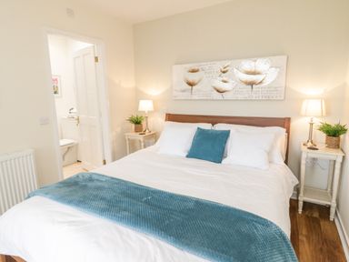A bedroom with a bed with white linens and teal throw at Beudy Hywel in Llanrug near Llanberis