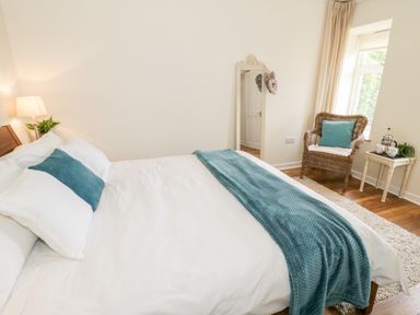 A bedroom with a made bed a rattan chair with a cushion a standing mirror and a small table with a tea set at Beudy Hywel Llanrug near Llanberis
