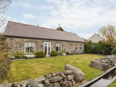 A stone house with a tiled roof and a garden with grass and bushes at Beudy Hywel in Llanrug near Llanberis