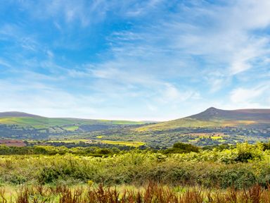 A landscape with hills and fields under a blue sky at Bwthyn Bach in Newport