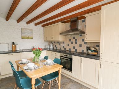 A kitchen with wooden table and chairs a vase of flowers and cream cabinets at Bwthyn Bach in Newport