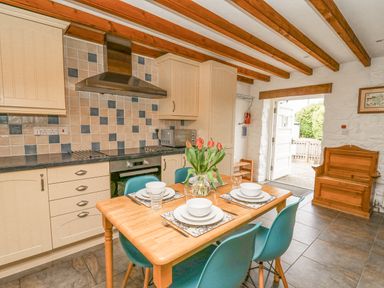 A kitchen with wooden table set for four blue chairs and cabinets with tiled backsplash at Bwthyn Bach in Newport