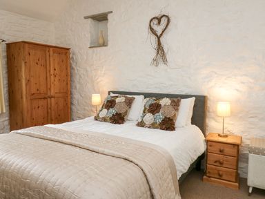 A bedroom with a double bed two bedside tables with lamps a wooden wardrobe and a heart-shaped wall decoration at Bwthyn Bach in Newport