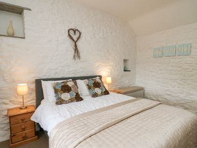 A bedroom with a bed with two floral pillows two bedside tables with lamps and white stone walls at Bwthyn Bach in Newport