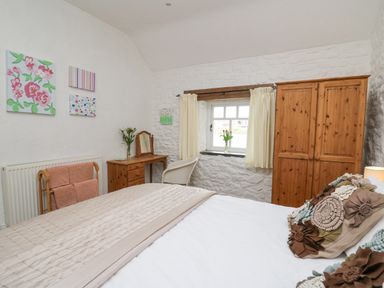 A bedroom with a bed a wooden wardrobe a dressing table and wall art at Bwthyn Bach in Newport