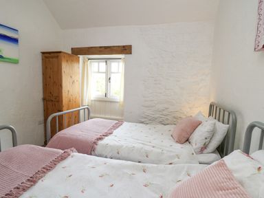 A bedroom with two metal frame single beds wooden wardrobe and a window with curtains at Bwthyn Bach in Newport