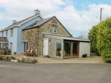 A stone and blue house with a gravel area and chairs outside at Y Cwtch in Newport
