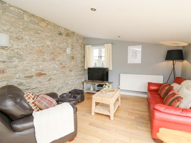 A living room with a red sofa a brown armchair a woven coffee table and a television on a stand at Y Cwtch in Newport