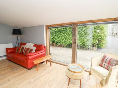 A living room with a red sofa and a beige armchair near large windows showing a hedge outside at Y Cwtch in Newport