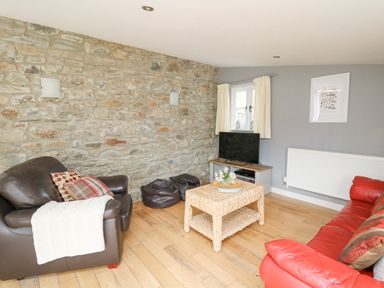 A living room with a stone wall a brown armchair a red sofa a wicker coffee table and a television at Y Cwtch in Newport